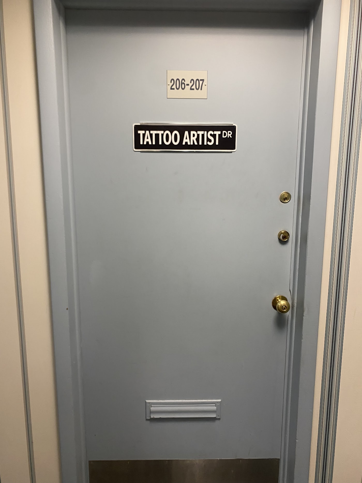 The studio entrance, a door marked Suites 206 to 207 with a Tattoo Artist Dr street-sign plaque